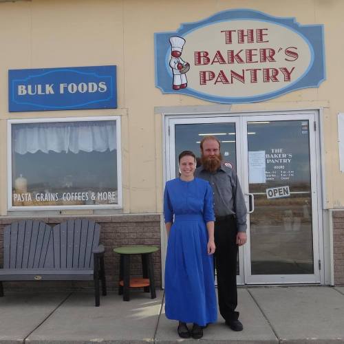 A woman in a blue dress and a man in a gray shirt stand outside "The Baker's Pantry" store.