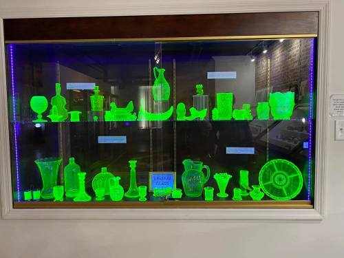 A display case filled with glowing green glassware and decorative items, illuminated under blue lighting.