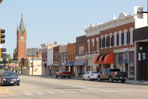A street view featuring historic buildings, shops, and a clock tower in the background on a clear day.