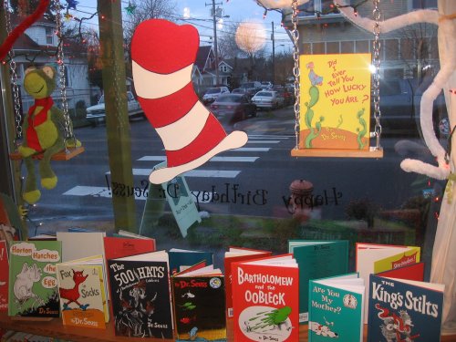 A colorful display of Dr. Seuss books in a window, featuring a large Cat in the Hat hat and festive decorations.