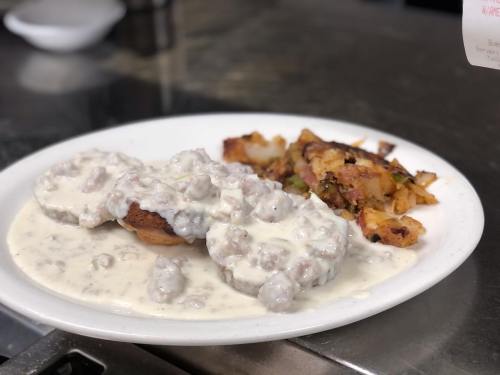 A plate of biscuits topped with creamy sausage gravy, served with a side of crispy hash browns.