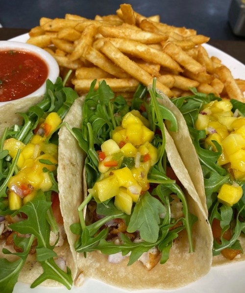 Three tacos filled with arugula and mango salsa, served with a side of fries and salsa.
