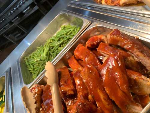 A close-up of a buffet tray with barbecue ribs in sauce and a side of green beans.