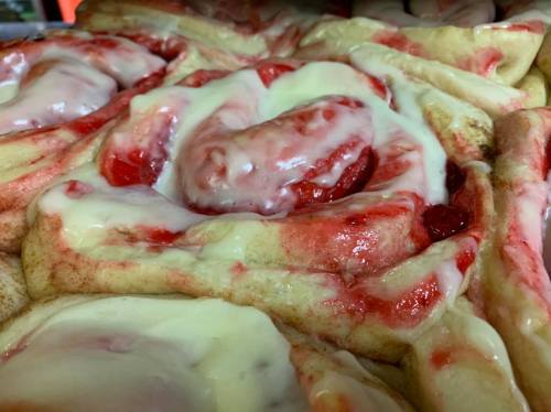 Close-up of freshly baked cinnamon rolls with cream cheese frosting and a swirl of cherry filling.