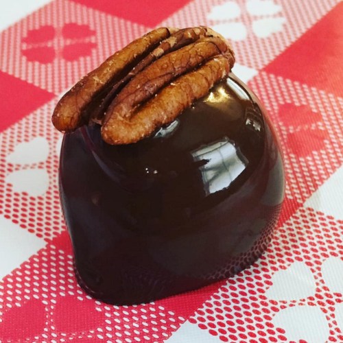 A glossy chocolate treat topped with a pecan, resting on a red and white patterned surface.