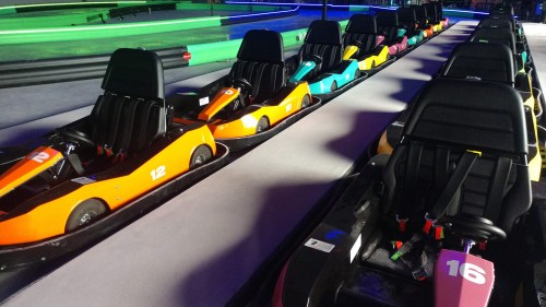 A row of colorful go-karts lined up on a track, ready for racing in a vibrant indoor setting.