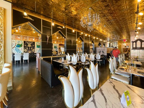 Elegant restaurant interior with gold accents, ornate decor, and stylish seating. A staff member is visible in the background.
