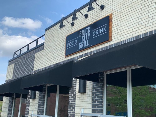 Sign for "Brick City Grill" featuring "Food" and "Drink" on a brick building with awnings.