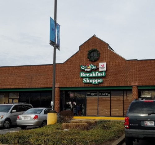 Exterior of a Breakfast Shoppe with a festive wreath, featuring a sign and parked cars in front.
