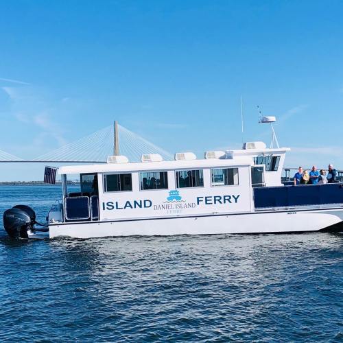 A ferry named "Daniel Island Ferry" navigates the water with a bridge in the background under a clear blue sky.