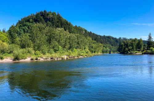 A serene river flows through lush greenery, with a hill in the background under a clear blue sky.