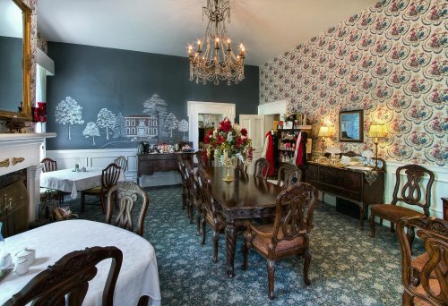 Elegant dining room with a large table, floral wallpaper, chandelier, and decorative fireplace.