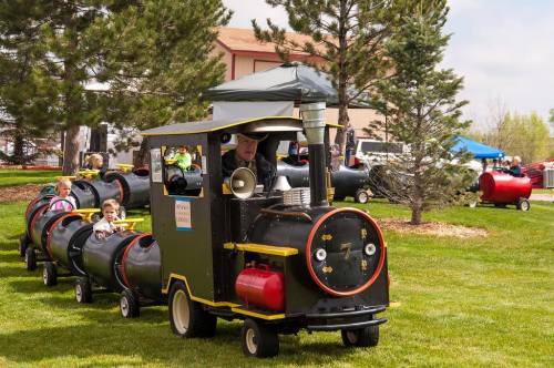 A small train ride for children, with a black engine and colorful cars, set in a grassy park with trees.