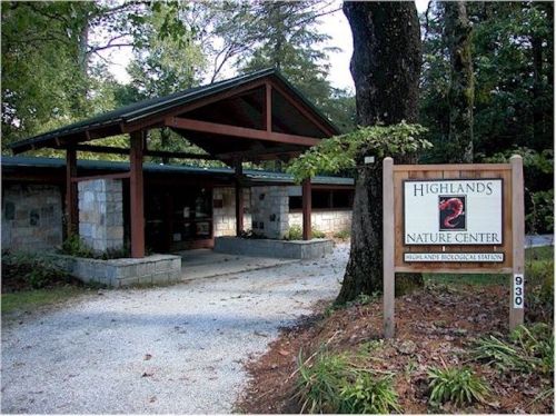 A stone and wood building with a sloped roof, surrounded by trees, featuring a sign for Highlands Nature Center.