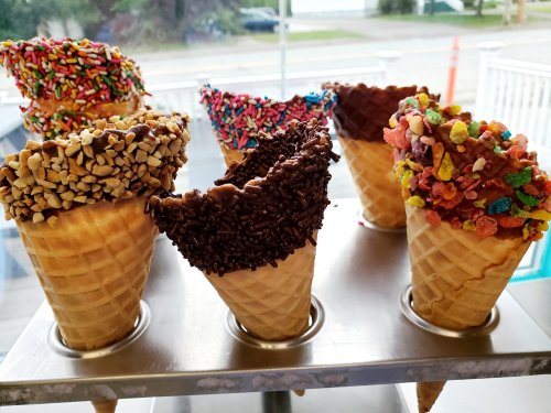 A display of ice cream cones with various toppings, including sprinkles, nuts, and chocolate, in a metal holder.