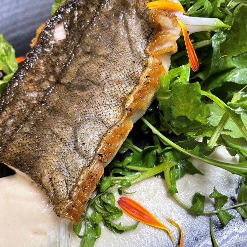 A close-up of a seared fish fillet on a bed of fresh greens, garnished with edible flowers.