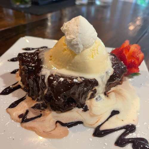 A decadent brownie topped with vanilla ice cream, whipped cream, and a strawberry, drizzled with chocolate sauce.