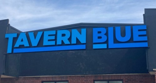 Sign for "TAVERN BLUE" in bold blue letters against a dark background.