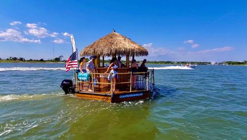 A tiki-style boat with people enjoying a sunny day on the water, surrounded by blue skies and gentle waves.