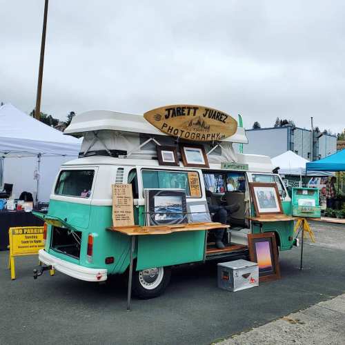 A vintage camper van set up as a photography booth, displaying framed photos at an outdoor market.