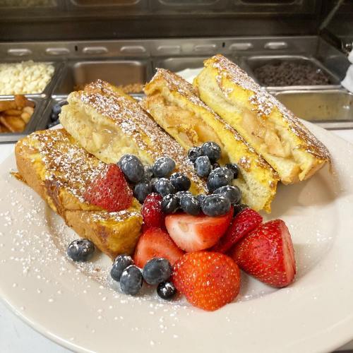 Plate of French toast topped with powdered sugar, surrounded by fresh strawberries and blueberries.