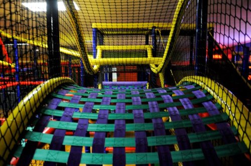 Colorful indoor play structure with netting and woven mats, featuring slides and climbing areas.