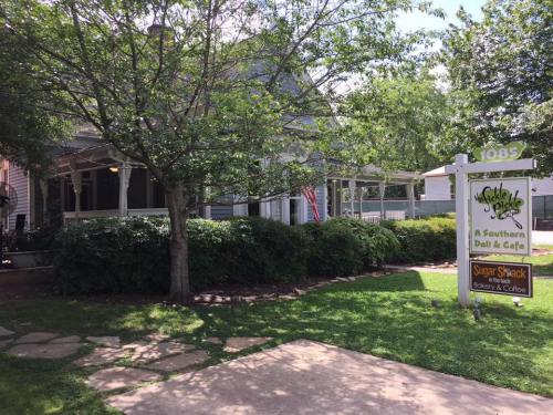A charming Southern deli and café with a sign, surrounded by greenery and a pathway leading to the entrance.