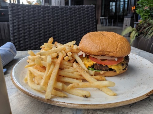 A juicy cheeseburger with lettuce, tomato, and onions, served with a side of crispy French fries on a plate.