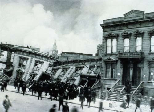 Historic photo of a city street after an earthquake, featuring tilted buildings and crowds of people.
