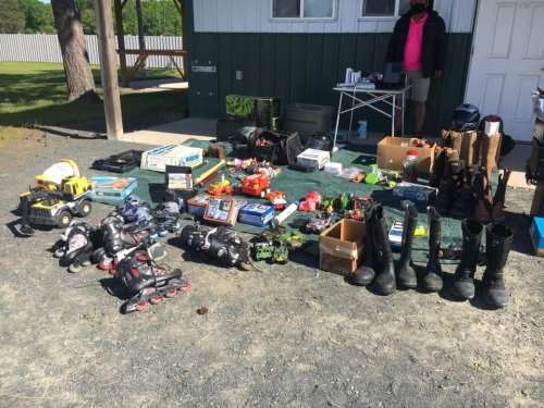 A variety of items for sale at a yard sale, including toys, shoes, and tools, displayed on a gravel surface.