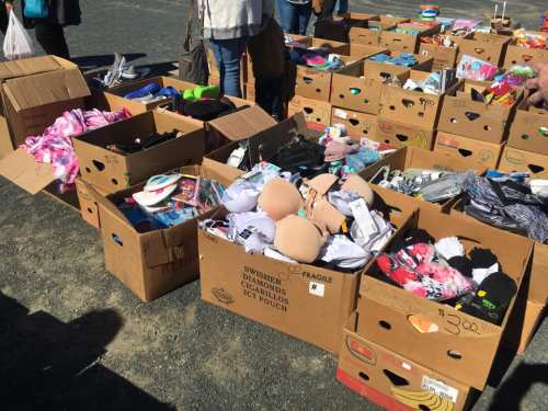 Boxes filled with assorted clothing items, including bras and accessories, at an outdoor market.