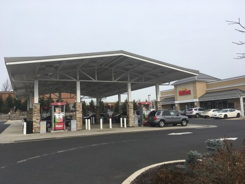 A Wawa gas station with multiple pumps and a convenience store, surrounded by trees and parked cars.
