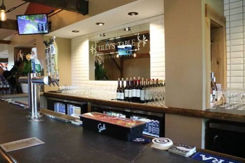 A bar area with a wooden counter, wine bottles, glasses, and a TV screen in a cozy setting.