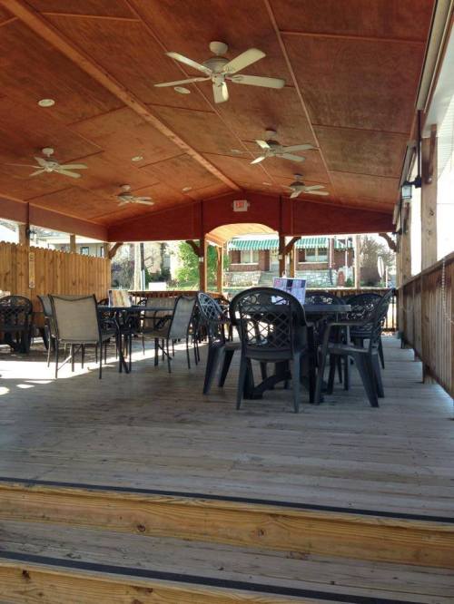 A spacious outdoor dining area with wooden floors, ceiling fans, and empty tables under a covered patio.