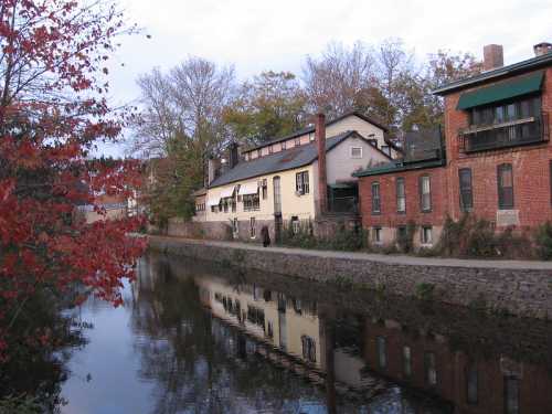 A serene canal scene with autumn foliage, reflecting historic buildings along the water's edge.