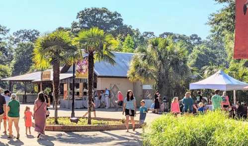 A lively outdoor market scene with families, palm trees, and tents under a clear blue sky.