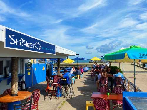 Outdoor dining area at a beachside restaurant with colorful umbrellas and patrons enjoying the sunny weather.