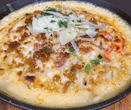 A creamy, baked pasta dish topped with cheese, breadcrumbs, and herbs, served in a skillet.