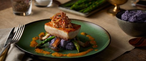 A beautifully plated dish featuring seared fish atop purple mashed potatoes, garnished with crispy onions and asparagus.