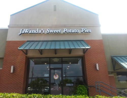 Sign for JaWanda's Sweet Potato Pies, featuring an open storefront with a welcoming entrance and greenery.