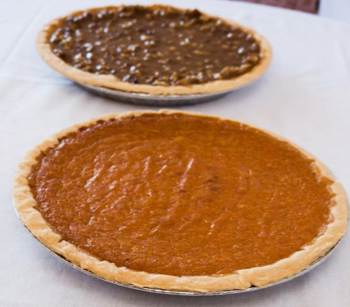 Two pies on a table: one pumpkin pie with a smooth orange filling and one pecan pie with a glossy brown topping.