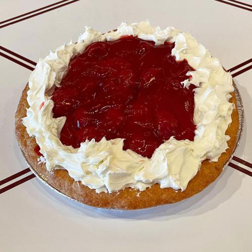 A cherry pie topped with whipped cream, featuring a golden crust and a glossy red cherry filling.