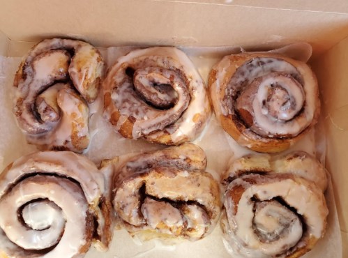 A box of six freshly baked cinnamon rolls topped with creamy icing.