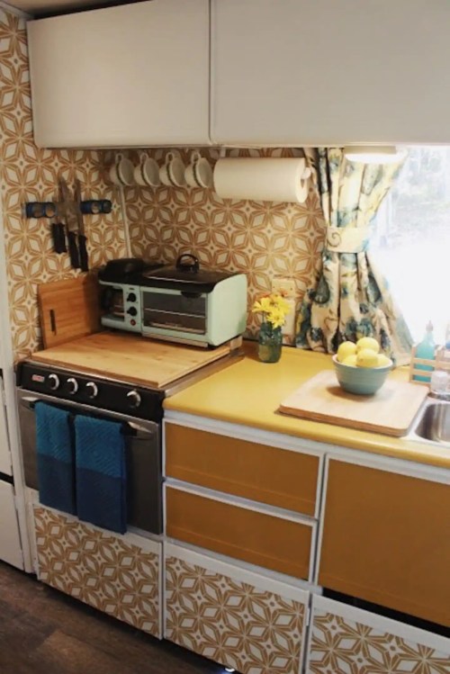 A cozy kitchen with patterned wallpaper, a wooden countertop, an oven, and colorful storage cabinets.