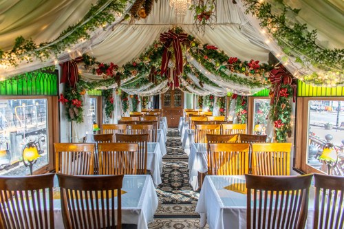 Elegant restaurant interior with decorated tables, draped fabric, and festive greenery, creating a cozy atmosphere.