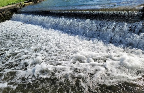 A close-up of a waterfall cascading over a stone edge, creating white foam in the water below.