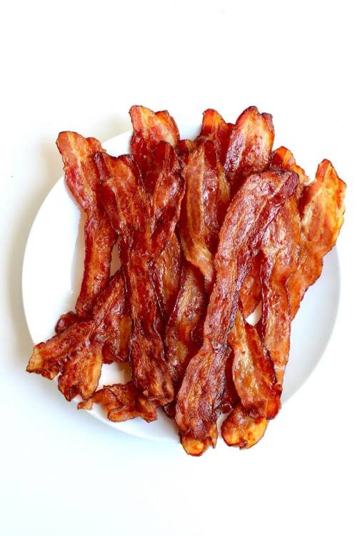 A white plate filled with crispy, golden-brown strips of bacon arranged neatly.