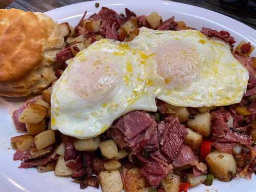 A plate of hash with diced potatoes, corned beef, and two sunny-side-up eggs, served with a biscuit on the side.