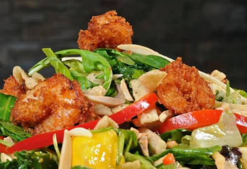 A vibrant salad topped with crispy shrimp, mixed greens, red peppers, and crunchy toppings.