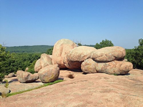 Large, smooth boulders on a rocky surface with green hills in the background under a clear blue sky.